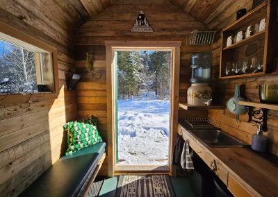 Intérieur de la cabane Le Poulailler avec porte ouverte sur la forêt enneigée, La Sôvageonne près du Mont-Tremblant