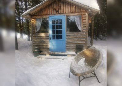 Extérieur de Jack's Camp en hiver avec porte bleue et fauteuil en osier, La Sôvageonne